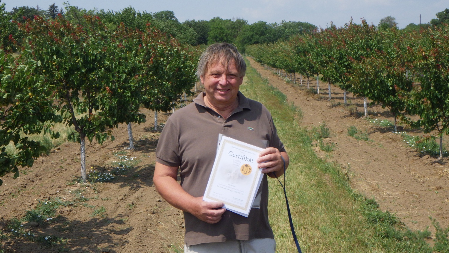 Pan Rotter s certifikátem o známce Sysli v sadu. V pozadí meruňkový sad, kde sysli žijí.
